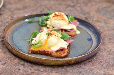 Dilimlenmiş jambon ve kremalı Hollandaise sosuyla kaplanmış kızarmış ekmeğin üzerinde mükemmel haşlanmış yumurta..