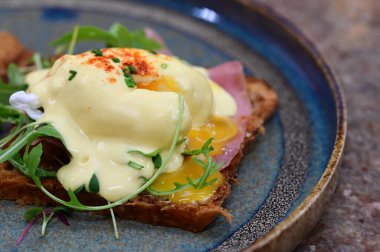 Dilimlenmiş jambon ve kremalı Hollandaise sosuyla kaplanmış kızarmış ekmeğin üzerinde mükemmel haşlanmış yumurta..