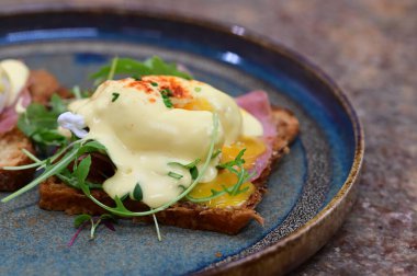 Dilimlenmiş jambon ve kremalı Hollandaise sosuyla kaplanmış kızarmış ekmeğin üzerinde mükemmel haşlanmış yumurta..