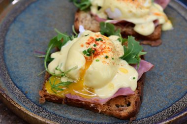 Dilimlenmiş jambon ve kremalı Hollandaise sosuyla kaplanmış kızarmış ekmeğin üzerinde mükemmel haşlanmış yumurta..