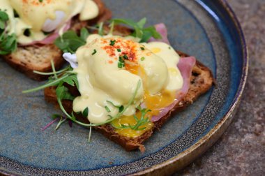 Dilimlenmiş jambon ve kremalı Hollandaise sosuyla kaplanmış kızarmış ekmeğin üzerinde mükemmel haşlanmış yumurta..
