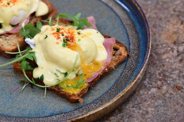 Dilimlenmiş jambon ve kremalı Hollandaise sosuyla kaplanmış kızarmış ekmeğin üzerinde mükemmel haşlanmış yumurta..