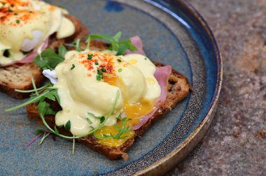 Dilimlenmiş jambon ve kremalı Hollandaise sosuyla kaplanmış kızarmış ekmeğin üzerinde mükemmel haşlanmış yumurta..
