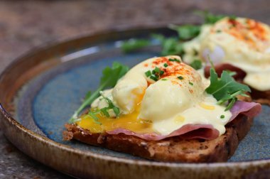 Dilimlenmiş jambon ve kremalı Hollandaise sosuyla kaplanmış kızarmış ekmeğin üzerinde mükemmel haşlanmış yumurta..