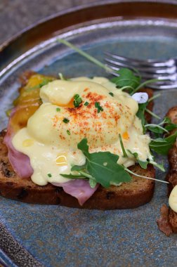 Dilimlenmiş jambon ve kremalı Hollandaise sosuyla kaplanmış kızarmış ekmeğin üzerinde mükemmel haşlanmış yumurta..