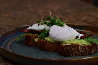 Kavrulmuş yumurtalı avokado tostu, pastırma ve mikroyeşillik gurmesi. Yakın plan kahvaltı.