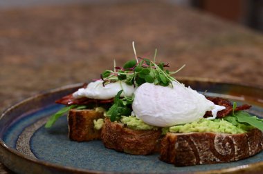 Kavrulmuş yumurtalı avokado tostu, pastırma ve mikroyeşillik gurmesi. Yakın plan kahvaltı.