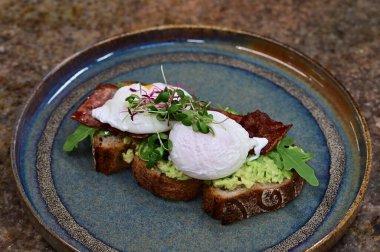 Kavrulmuş yumurtalı avokado tostu, pastırma ve mikroyeşillik gurmesi. Yakın plan kahvaltı.