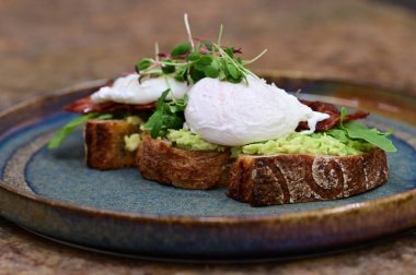 Kavrulmuş yumurtalı avokado tostu, pastırma ve mikroyeşillik gurmesi. Yakın plan kahvaltı.