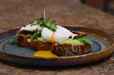 Kavrulmuş yumurtalı avokado tostu, pastırma ve mikroyeşillik gurmesi. Yakın plan kahvaltı.