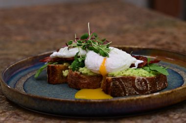 Kavrulmuş yumurtalı avokado tostu, pastırma ve mikroyeşillik gurmesi. Yakın plan kahvaltı.