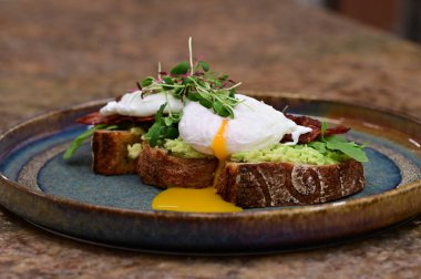 Kavrulmuş yumurtalı avokado tostu, pastırma ve mikroyeşillik gurmesi. Yakın plan kahvaltı.