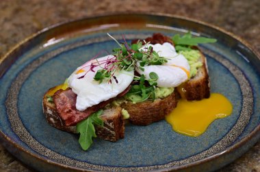 Kavrulmuş yumurtalı avokado tostu, pastırma ve mikroyeşillik gurmesi. Yakın plan kahvaltı.