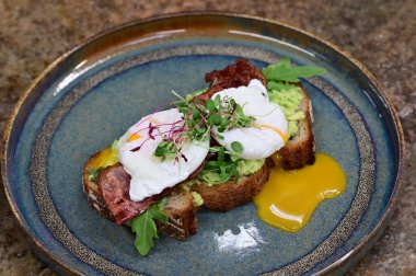 Kavrulmuş yumurtalı avokado tostu, pastırma ve mikroyeşillik gurmesi. Yakın plan kahvaltı.