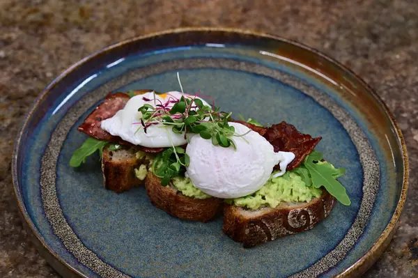 Kavrulmuş yumurtalı avokado tostu, pastırma ve mikroyeşillik gurmesi. Yakın plan kahvaltı.