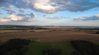 Dramatik bulutlar, tarımsal tarlalar, ormanlar ve çayırlarla Çek kırsalında güzel bir günbatımı. Sıcak akşam ışığı barışçıl, resim gibi bir atmosfer yaratır ve doğayı ön plana çıkarır.