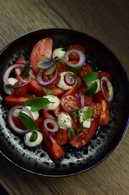 Siyah tabakta soğanlı ve fesleğenli domates.