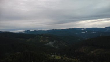 aerial drone photo of a mountain landscape with forest and clouds.