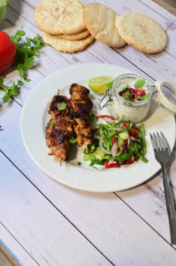 Chicken kebab served with raita and fresh salad on a white plate, light background, healthy and delicious popular meal.