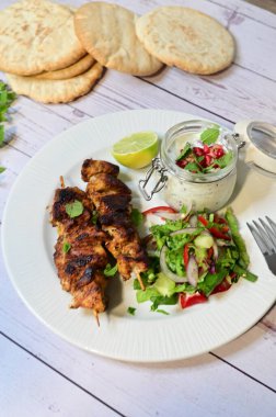 Chicken kebab served with raita and fresh salad on a white plate, light background, healthy and delicious popular meal.