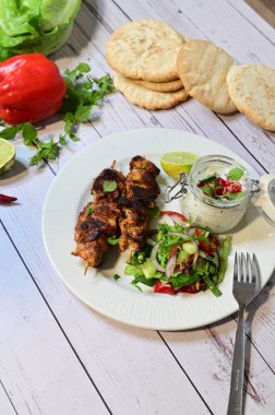 Chicken kebab served with raita and fresh salad on a white plate, light background, healthy and delicious popular meal.