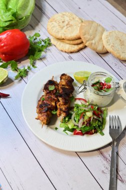 Chicken kebab served with raita and fresh salad on a white plate, light background, healthy and delicious popular meal.