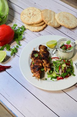 Chicken kebab served with raita and fresh salad on a white plate, light background, healthy and delicious popular meal.