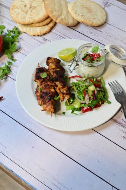 Chicken kebab served with raita and fresh salad on a white plate, light background, healthy and delicious popular meal.