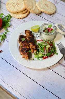Chicken kebab served with raita and fresh salad on a white plate, light background, healthy and delicious popular meal.