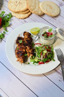 Chicken kebab served with raita and fresh salad on a white plate, light background, healthy and delicious popular meal.