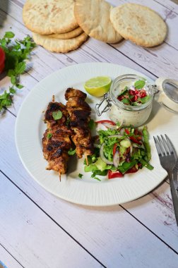Chicken kebab served with raita and fresh salad on a white plate, light background, healthy and delicious popular meal.