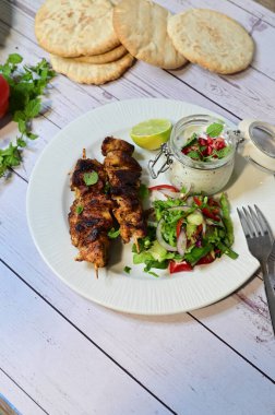 Chicken kebab served with raita and fresh salad on a white plate, light background, healthy and delicious popular meal.