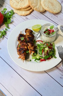 Chicken kebab served with raita and fresh salad on a white plate, light background, healthy and delicious popular meal.