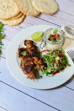 Chicken kebab served with raita and fresh salad on a white plate, light background, healthy and delicious popular meal.