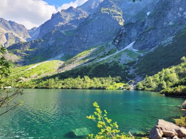 Güzel bir manzara - dağlar, güneşli bir günde, bir dağ gölünün turkuaz suyuna yansıyor.