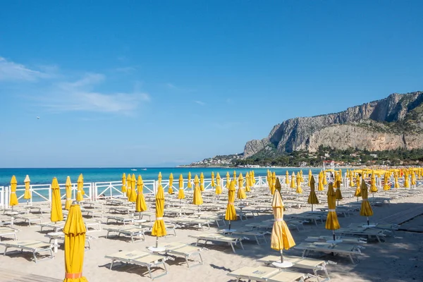 stock image Mondello sand beach with closed colored beach umbrellas in the summer sun and transparent turquoise blue sea. Vacation spot in Sicily, Palermo beach. Mondello, Palermo, Italy