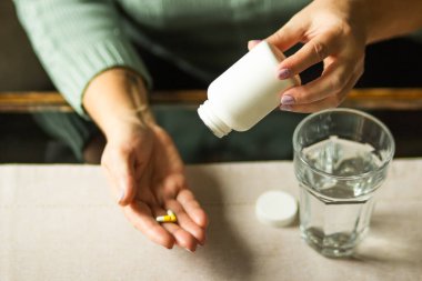 Elinde haplı beyaz plastik şişe ve elinde iki kapsül olan yaşlı bir kadın bir bardak suyla ilave haplar almaya hazır. Hasta kıdemli kadın ilaç alıyor. Sağlık hizmeti kavramı.