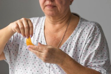 Yaşlı kadınların elleri önünde sarı hidrojel göz bantlarını tutuyor, kullanıma hazır. Yaşlı bayan kırışıklıklara ve şişkinliklere karşı kozmetik kullanıyor, günlük sabah rutini. Yaşlanma ve cilt bakımı.