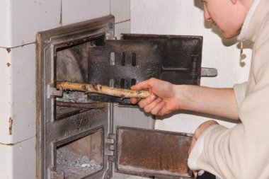 Zavallı yetişkin adam evdeki eski sobaya yakacak odun, huş ağacı dalları koyuyor. Adamın eli odun yakan fırına odun koyuyor. Soğuk kış gününde evi ısıtmak. Yoksulluk ve enerji krizi kavramı.