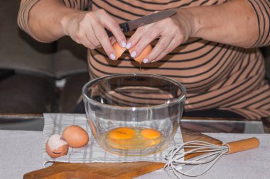 Yaşlı kadının elleri bıçakla cam kaseye yumurta kırıyor. Kahvaltı için omlet ya da krep yapmaya hazırlan. Tahta kesme tahtasına ve masa arkasına izole edilmiş bir kase taze yumurta ve kırbaç..