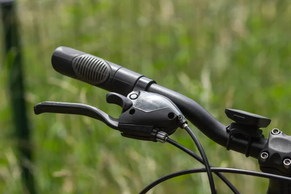 Close-up of black bicycle handlebar with brakes. Mountain sport bicycle on the green nature background. Summer time outdoor leisure activity. Sport and travel concept. Healthy active lifestyle.