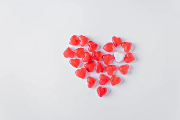 The whole heart consists of red heart-shaped jelly candies with one white jelly heart. Isolated on a white background. Valentine\'s Day concept. Space for text. Top view. Horizontal photo.