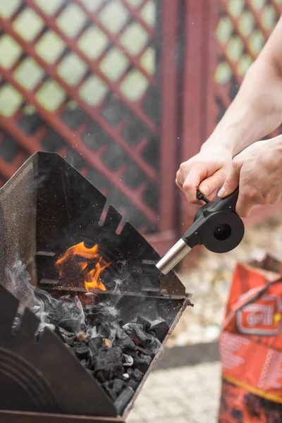 男の手を保持し 金属トレイ ポータブルグリルバーベキューで炭を火に送風機を使用しています バーベキューを設定します 友人との夏のレジャー活動 コテージの裏庭のピクニック — ストック写真