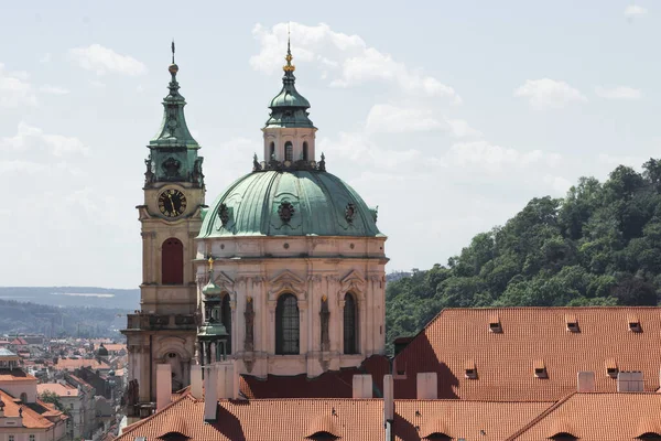 Çek Cumhuriyeti Prag 'daki Mala Strana bölgesinde saat kulesi olan eski Aziz Nicholas kilisesi. Prag 'ın eski kasabasının şehir manzarası. Kırmızı kiremitli çatılar, katedral kubbesi ve şehir parkı.