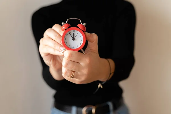 Woman\'s hands holds red alarm clock and sets the time. Businesswoman in black shirt adjusting or changing the time on vintage clock with bells. Time management concept. Time to start.