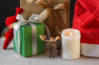 Yeni yıl ya da Noel kompozisyonu paketlenmiş hediye kutuları, oyuncak ren geyiği, yanan mum ve Noel Baba şapkası. Çelenk renkli Xmas titreşimleri. Kış tatiline hazırlık. Noel alışverişi ve satışları.