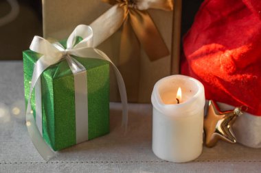 Yeni yıl ya da Noel kompozisyonu paketlenmiş hediye kutuları, yanan mum ve Noel Baba şapkası. Çelenk renkli Xmas titreşimleri. Kış tatiline hazırlık. Noel alışverişi ve satışları. 