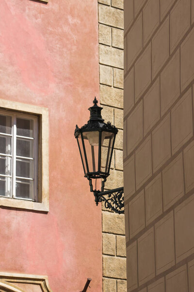Antique street lantern hanging on the corner of house wall in old town of Prague, Czech Republic. Old street light against pink wall in city center. Details of historic gas lamp. European tourism.