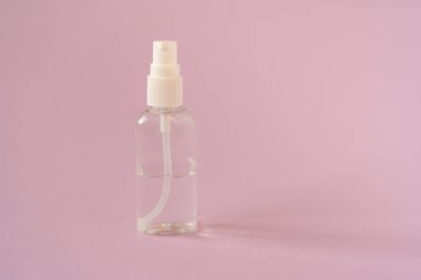 Üzerinde dezenfektan sıvısı olan şeffaf bir şişe, el dezenfektanı pembe arka tarafa izole edilmiş. Koronavirüs salgını sırasında el koruması. El temizliği kavramı.