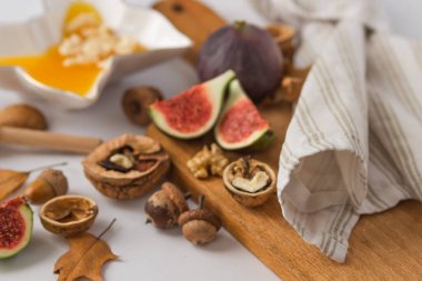 Kuru meşe yaprakları ve meşe palamudu ile süslenmiş tahta kesme tahtasının üzerinde dilimlenmiş olgun incirlerle, cevizlerle ve bal dolu tabakla dolu bir sonbahar natürmortu. Şarap için organik atıştırmalıklar. Sağlıklı beslenme.